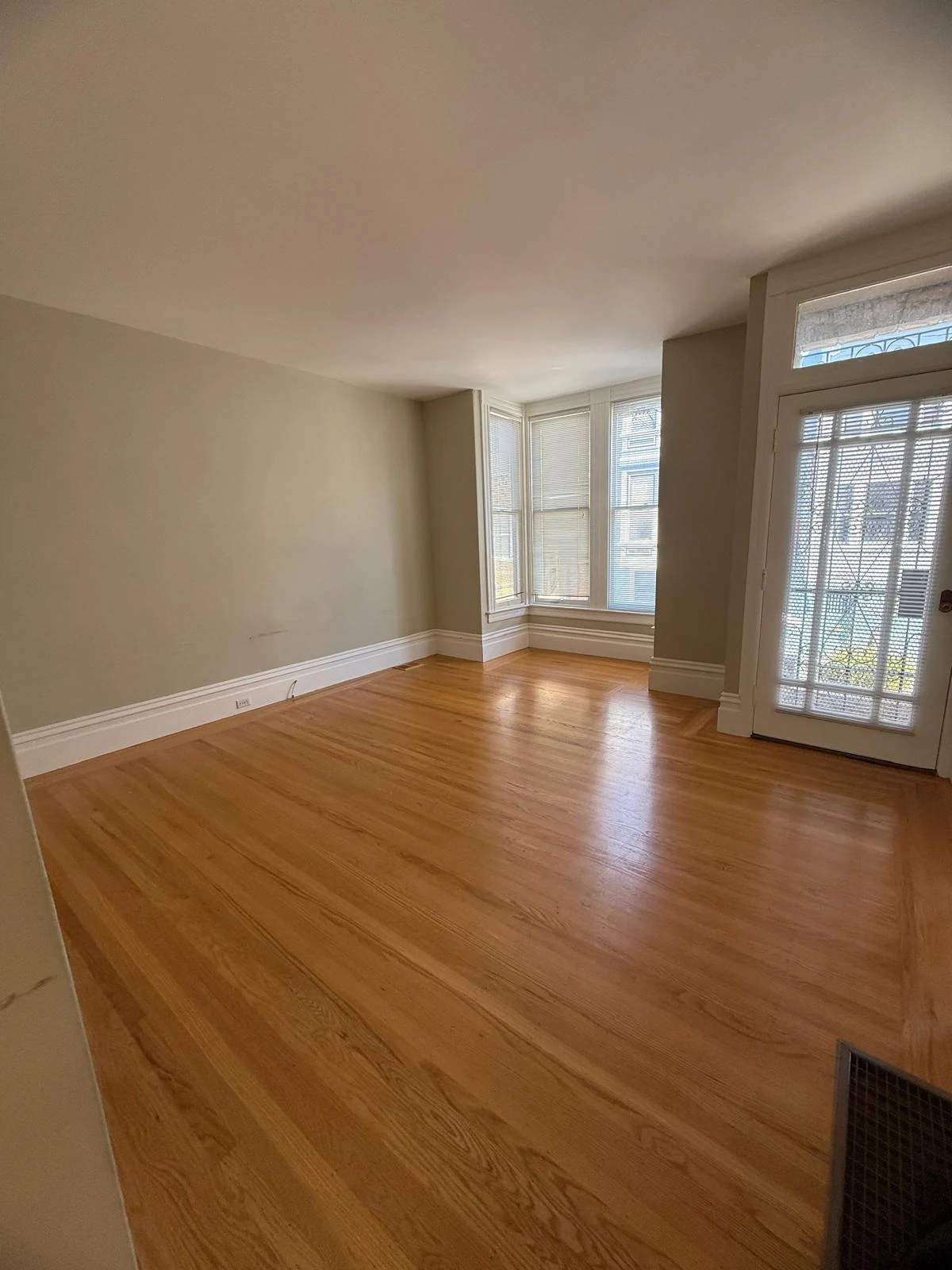 A room with warm hardwood floors, bay windows, and a glass door