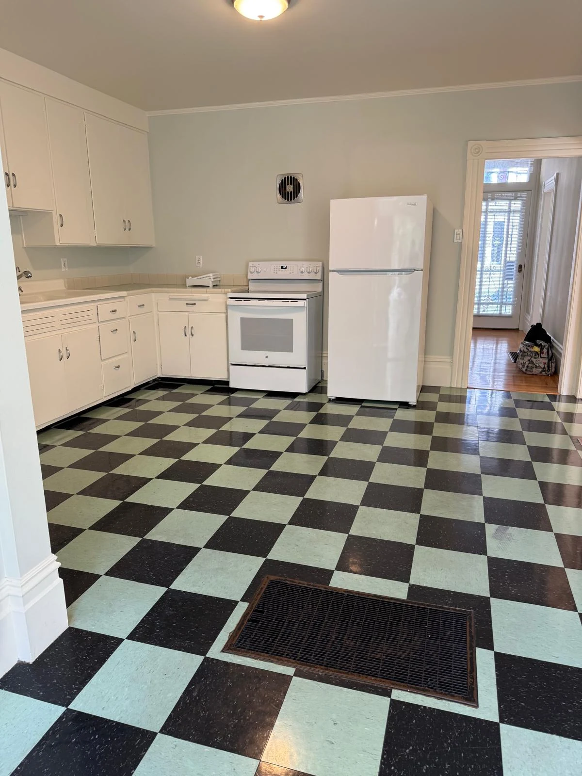A kitchen with white cabinets, a stove, a refrigerator, and a checkerboard floor