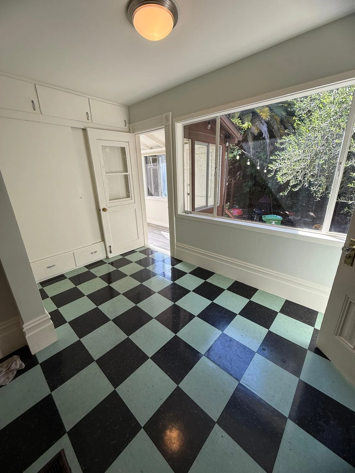 A room with white built-in cabinets, a large garden-facing window, and a checkerboard floor